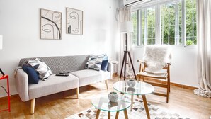 Olohuoneessa on sohva, lasinen sohvapöytä, tuoli ja seinällä taideteoksia.