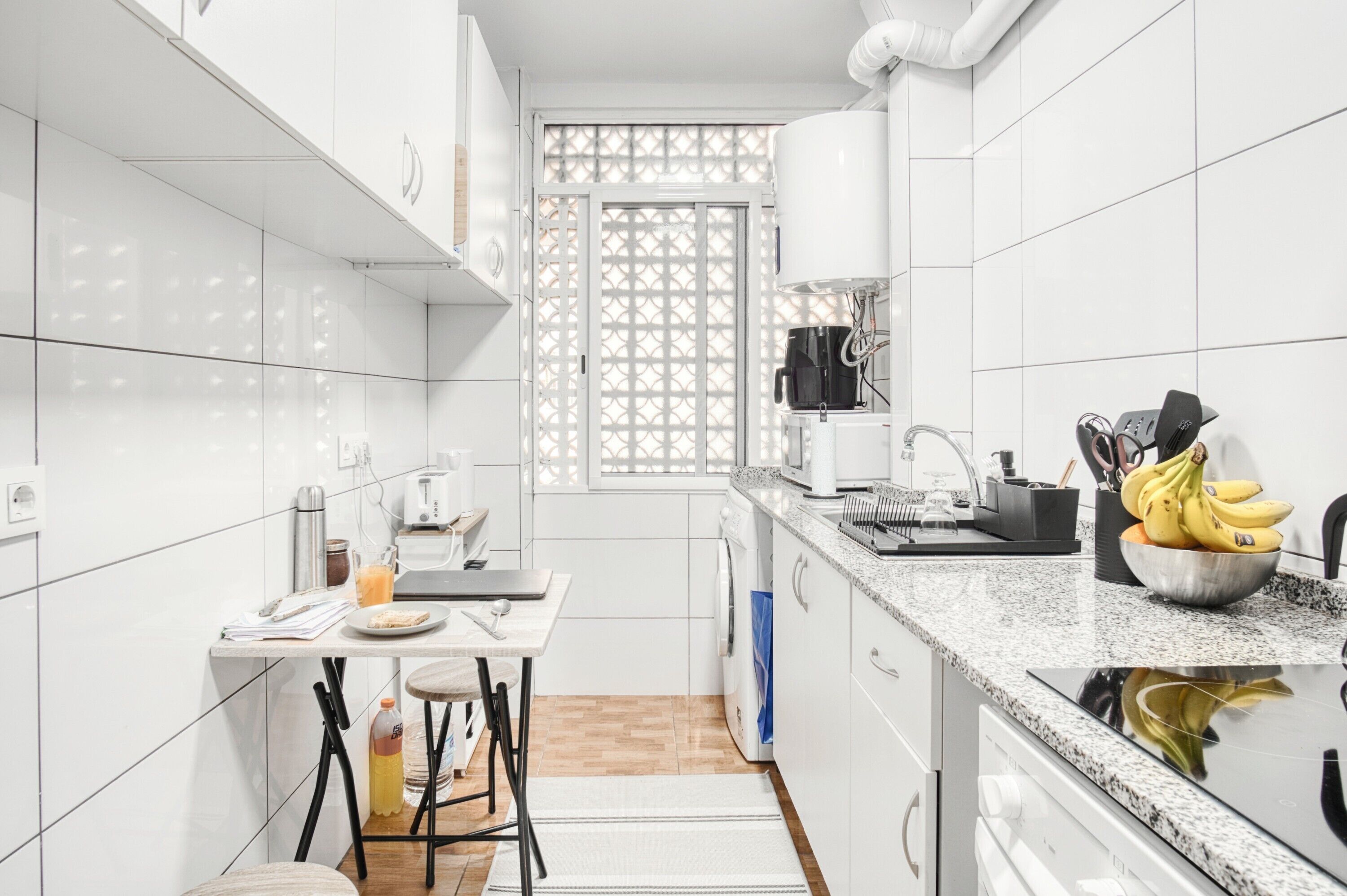 A modern kitchen with white cabinets, a coffee maker, a sink, and a countertop with a bowl of bananas.