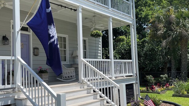 A two-story house with a porch, a flag, and a garden. - 1874 House. Walk Everywhere. Pets Welcome. (Beaufort)