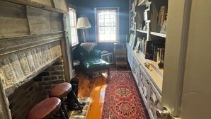 A cozy living room with a fireplace, a green sofa, a patterned rug, and a bookshelf. - 1874 House. Walk Everywhere. Pets Welcome. (Beaufort)