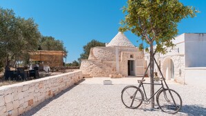 A stone building with a conical roof, a bicycle, and a seating area with tables and chairs.
