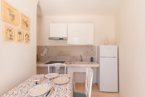 Une petite cuisine avec des meubles blancs, un évier, un réfrigérateur et une table à manger dressée avec des assiettes et des couverts.