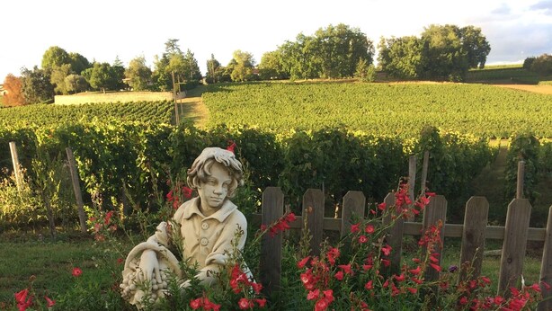 Un jardín con una estatua, un camino de grava y una valla.