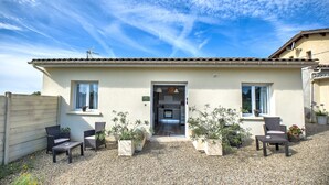 Ein Haus mit Ziegeldach, einer Haustür und einer kleinen Terrasse mit Gartenmöbeln und Blumentöpfen.