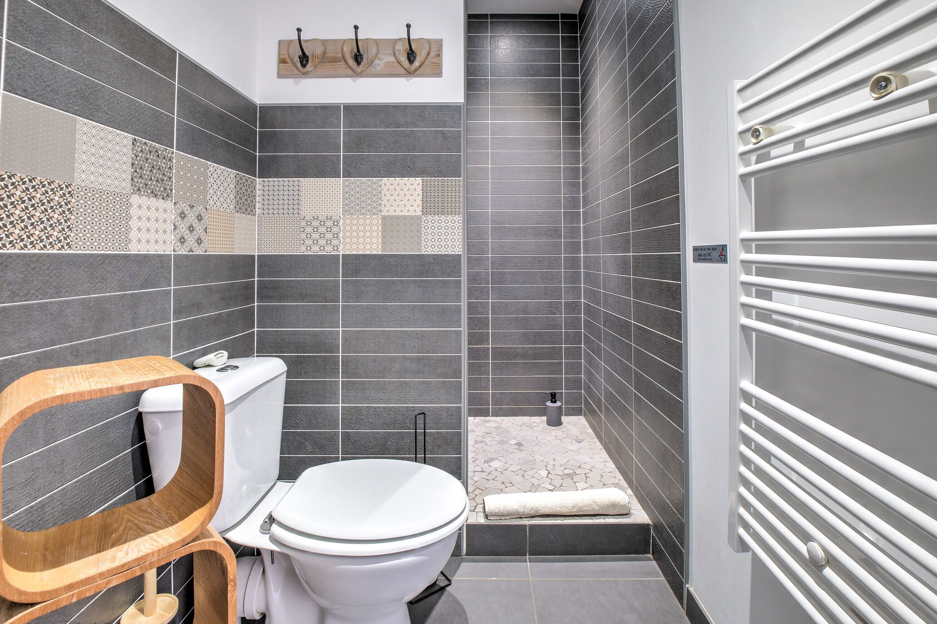 A modern bathroom with a toilet, a wooden vanity, a shower area, and a towel rack.