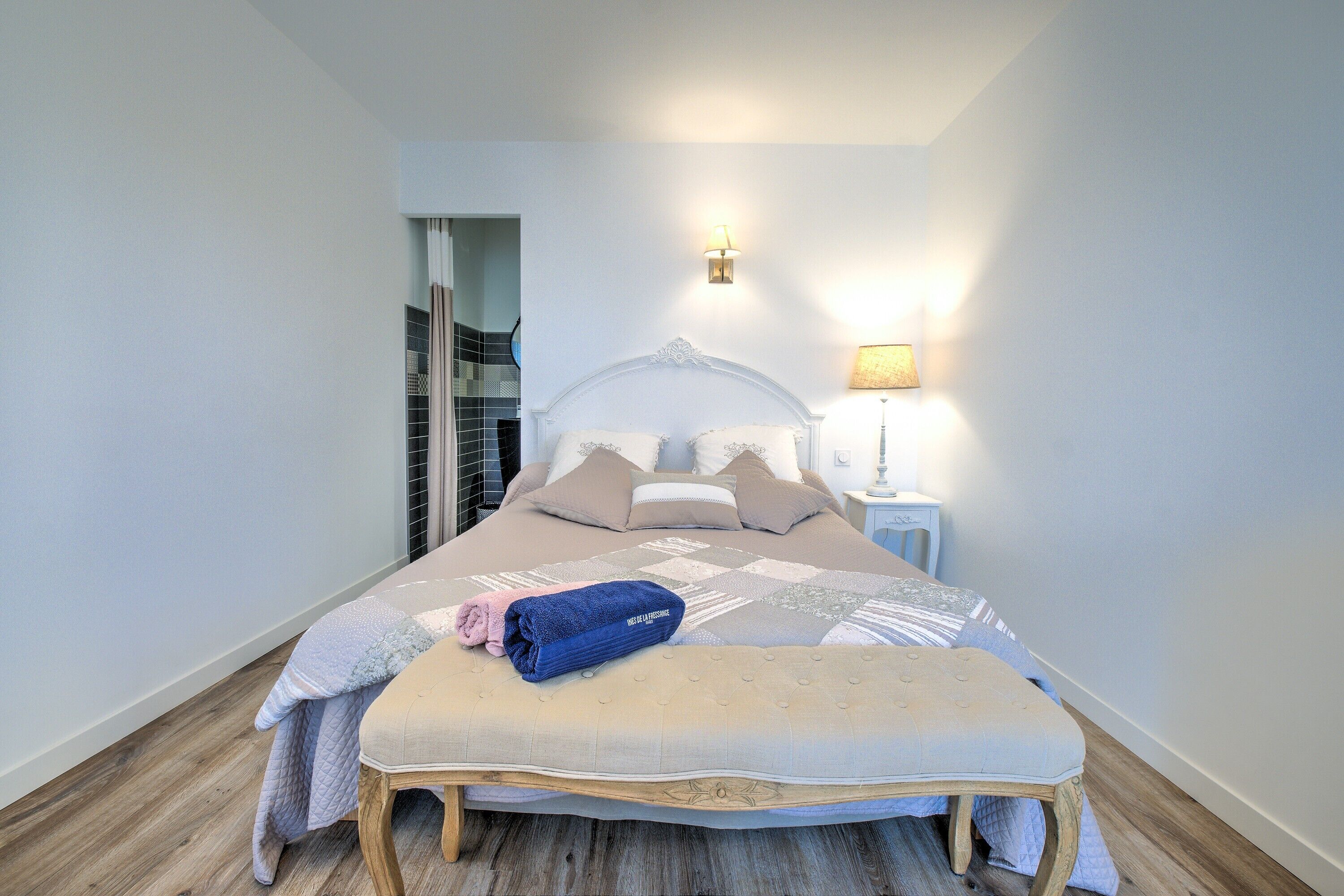 Un lit bien fait, avec une tête de lit, une lampe de chevet et un plancher en bois.