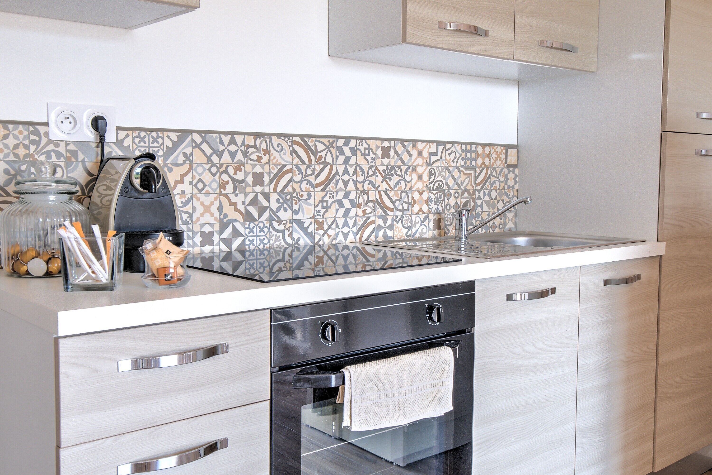 A modern kitchen with a patterned backsplash, stainless steel appliances, and light wood cabinetry.