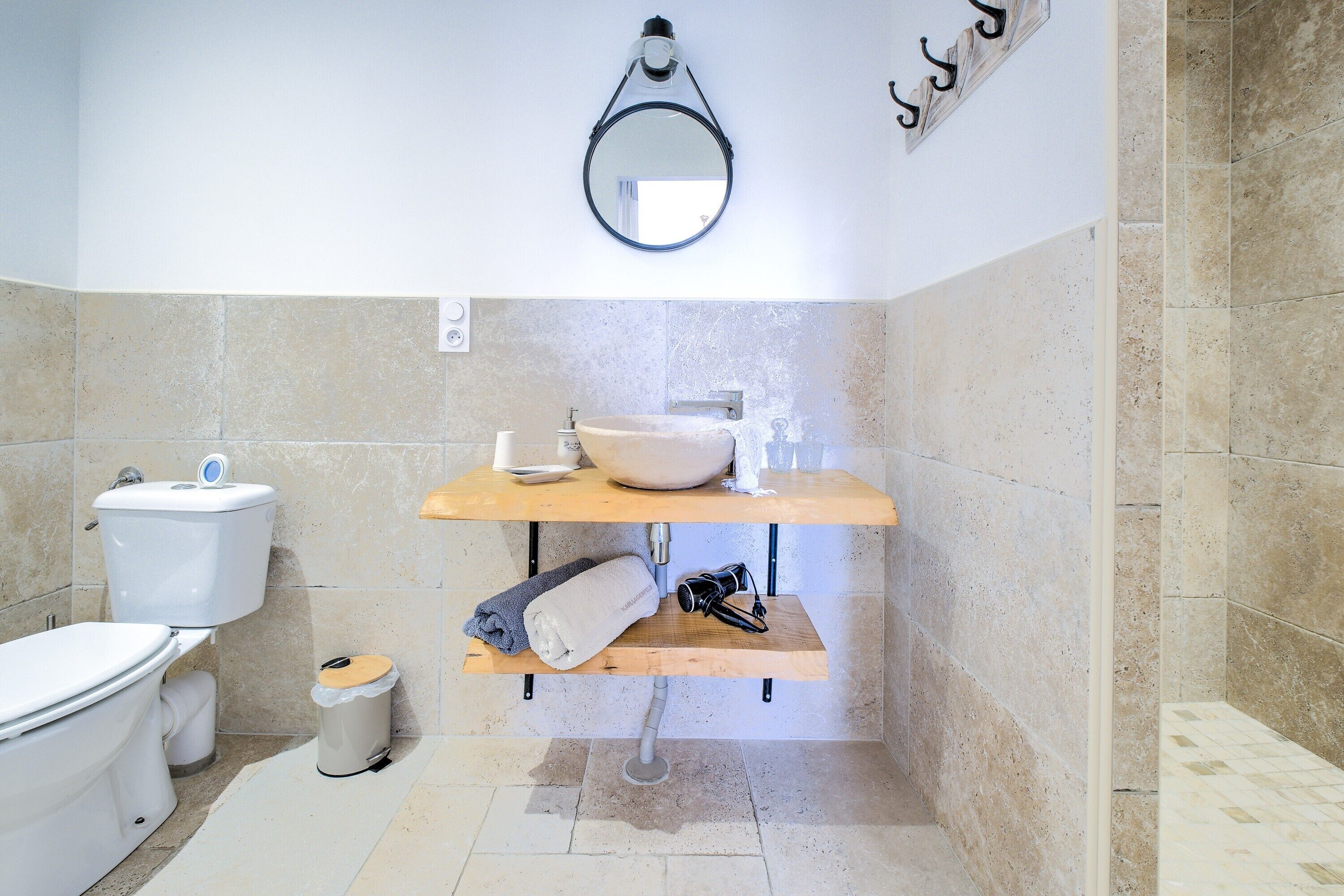 Un bagno con il water, un lavandino, uno specchio e uno scaffale con asciugamani e una tazza.