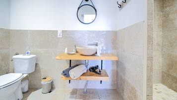 Un bagno con il water, un lavandino, uno specchio e uno scaffale con asciugamani e una tazza.