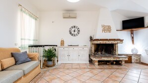 A living room with a sofa, a fireplace, a clock, and a television. - Villa 'Ivonne's' with Private Terrace, Wi-Fi and Air Conditioning (Villasimius)