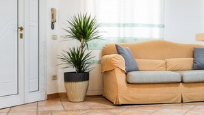 A room with a beige sofa, a potted plant, a telephone, and a door. - Villa 'Ivonne's' with Private Terrace, Wi-Fi and Air Conditioning (Villasimius)