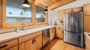 A modern kitchen with wooden cabinets, stainless steel appliances, and large windows. - Dune Ranch | Private Lake Michigan Beach + Fire Pit | Cathead Bay (Northport)