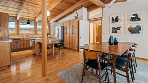 A spacious kitchen with wooden beams, a dining area with a large table and chairs, and a refrigerator. - Dune Ranch | Private Lake Michigan Beach + Fire Pit | Cathead Bay (Northport)