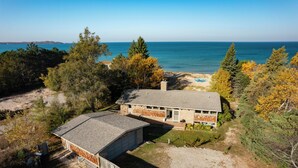 A two-story house with a garage, surrounded by trees and a view of the sea. - Dune Ranch | Private Lake Michigan Beach + Fire Pit | Cathead Bay (Northport)
