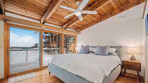 A bedroom with a large bed, wooden floor, ceiling fan, and a sliding glass door leading to a balcony. - Dune Ranch | Private Lake Michigan Beach + Fire Pit | Cathead Bay (Northport)