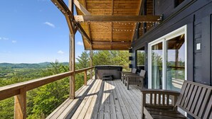 Eine Holzterrasse mit Whirlpool, Sitzgelegenheiten und Blick auf die Landschaft.