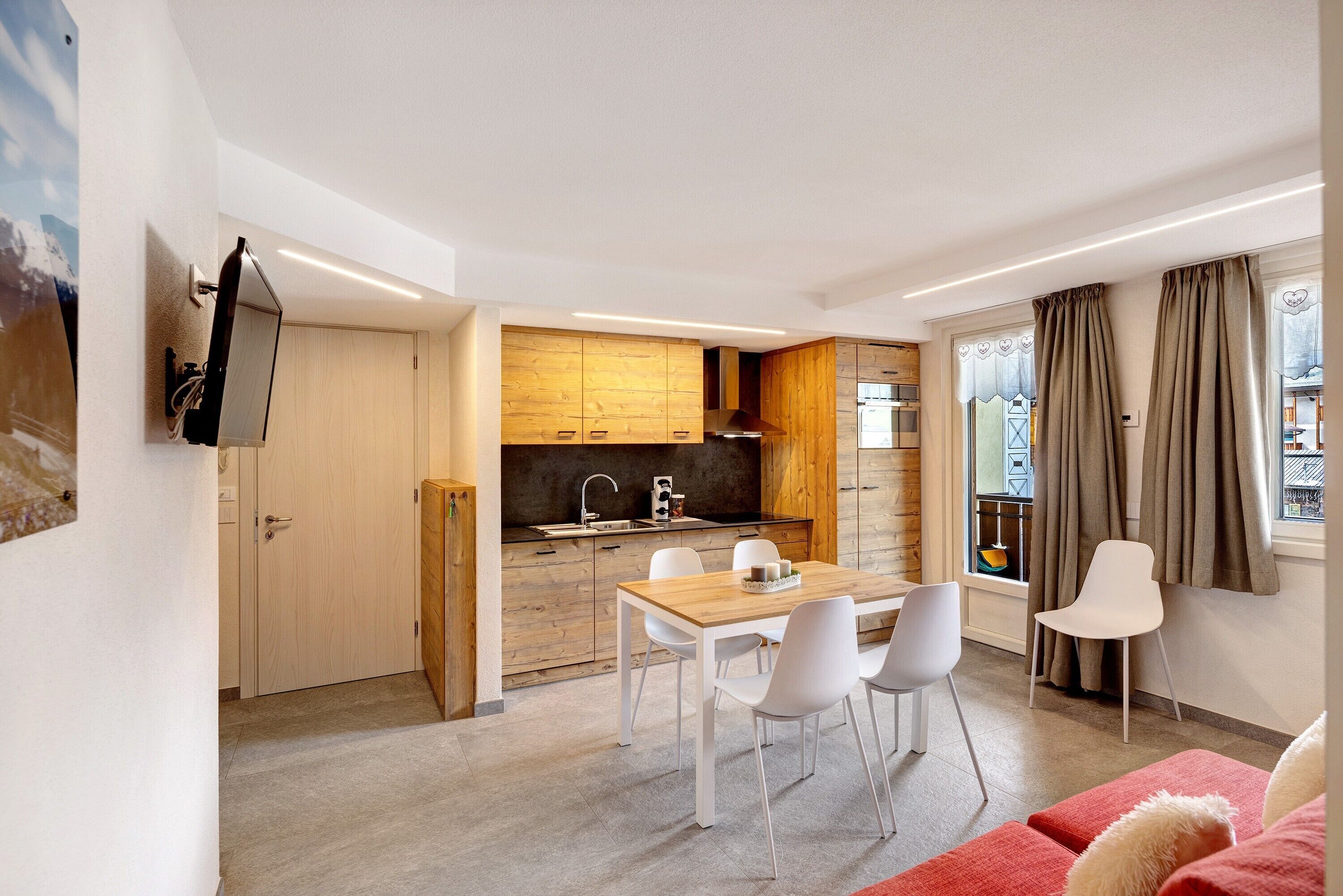 Eine moderne Küche mit Holzausstattung, ein Essbereich mit weißen Stühlen und ein rotes Sofa.