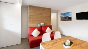 A modern room with a red sofa, white chairs, a wooden table, and a TV mounted on the wall. - Apartment 'A Due Passi Verde' with Mountain View, Balcony and Wi-Fi (Livigno)
