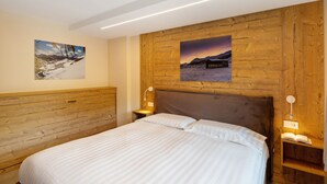 A bedroom with a wooden headboard, a bed with white linens, two bedside lamps, and two wall-mounted paintings. - Apartment 'A Due Passi Verde' with Mountain View, Balcony and Wi-Fi (Livigno)