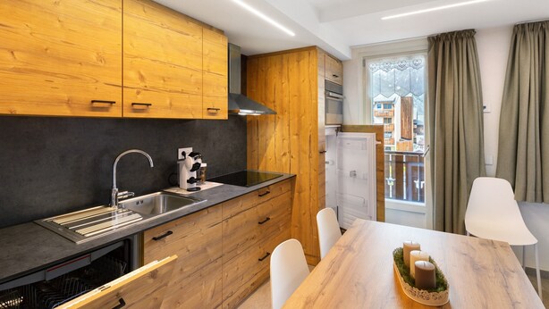 A modern kitchen with wooden cabinets, a stainless steel sink, and a dining area with a table and chairs. - Apartment 'A Due Passi Verde' with Mountain View, Balcony and Wi-Fi (Livigno)