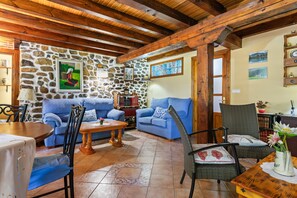 Una sala de estar acogedora con paredes de piedra, vigas de madera, sofás azules y una mesa de comedor.