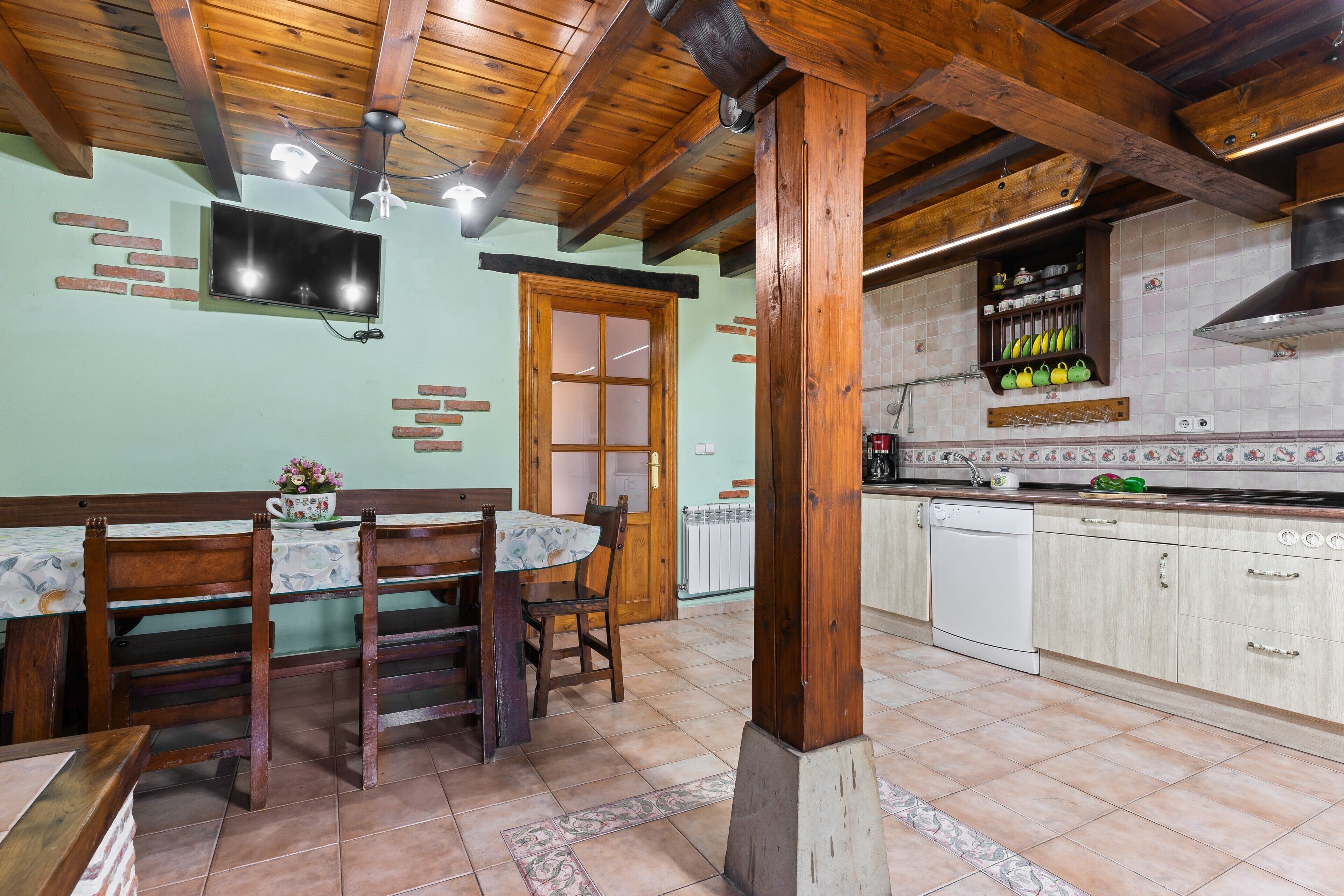 Una cucina con travi in legno, un'area pranzo con tavolo e sedie, ed un ripiano a muro con utensili da cucina.