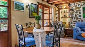 Un comedor con una mesa de madera, sillas, un florero con planta y una pared de piedra con estantes.