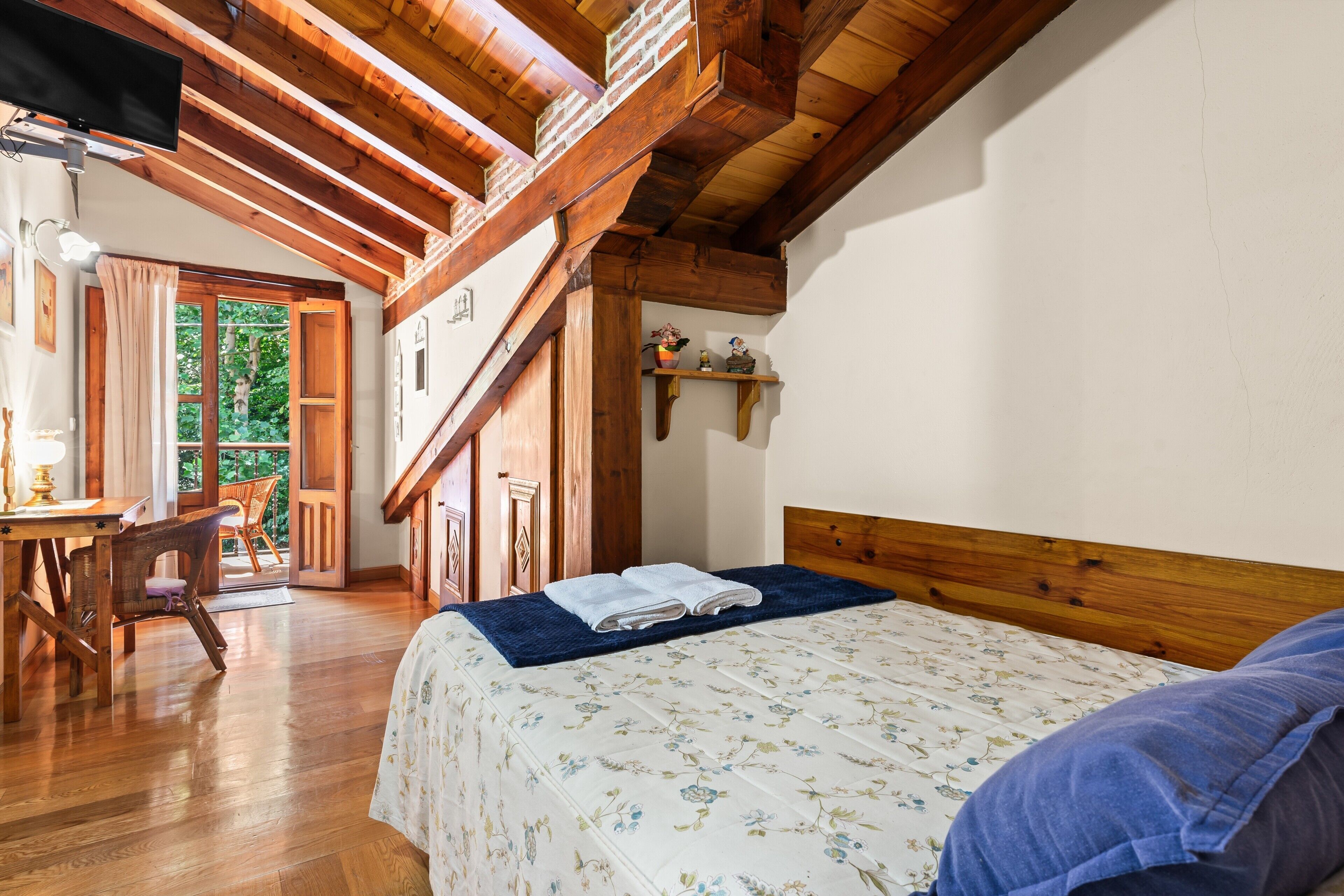 Ein Schlafzimmer mit Holzboden, einem Bett mit Blumenmuster-Bettdecke, einem Nachttisch aus Holz und Blick ins Freie.