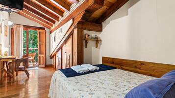 Ein Schlafzimmer mit Holzboden, einem Bett mit Blumenmuster-Bettdecke, einem Nachttisch aus Holz und Blick ins Freie.
