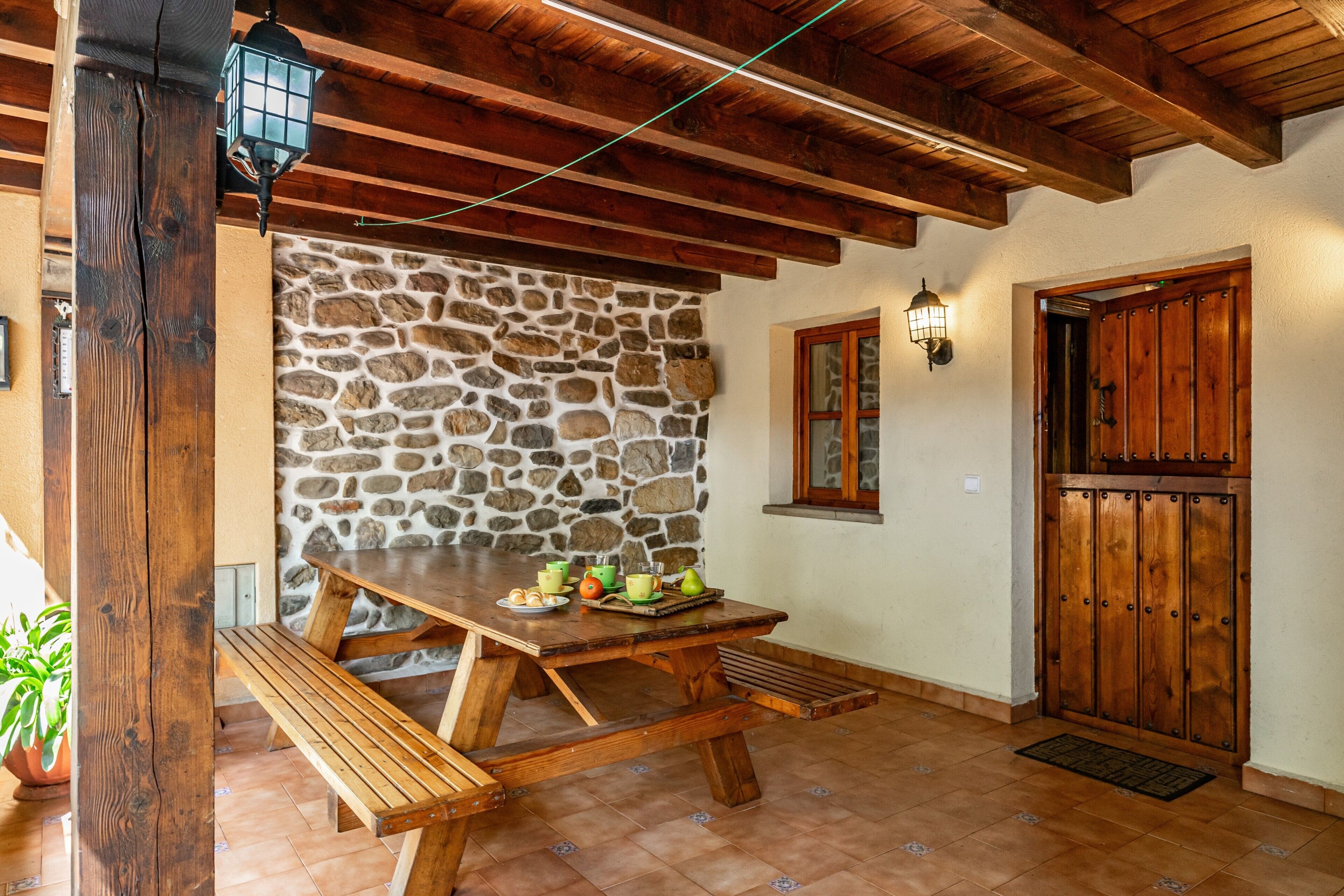 Une table en bois rustique, accompagnée de bancs, un mur en pierre, une porte en bois et un escalier en pierre.