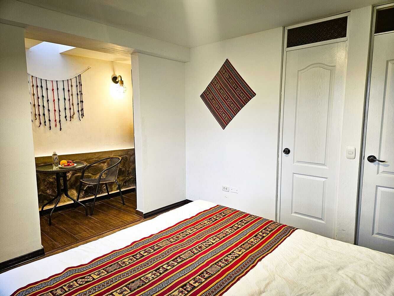 A bedroom with a bed, a chair, a table with fruit, a wall hanging, and a patterned rug.