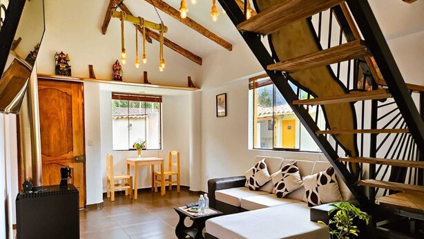 Un salon chaleureux avec un canapé, une table basse et un escalier dont les poutres en bois sont apparentes.