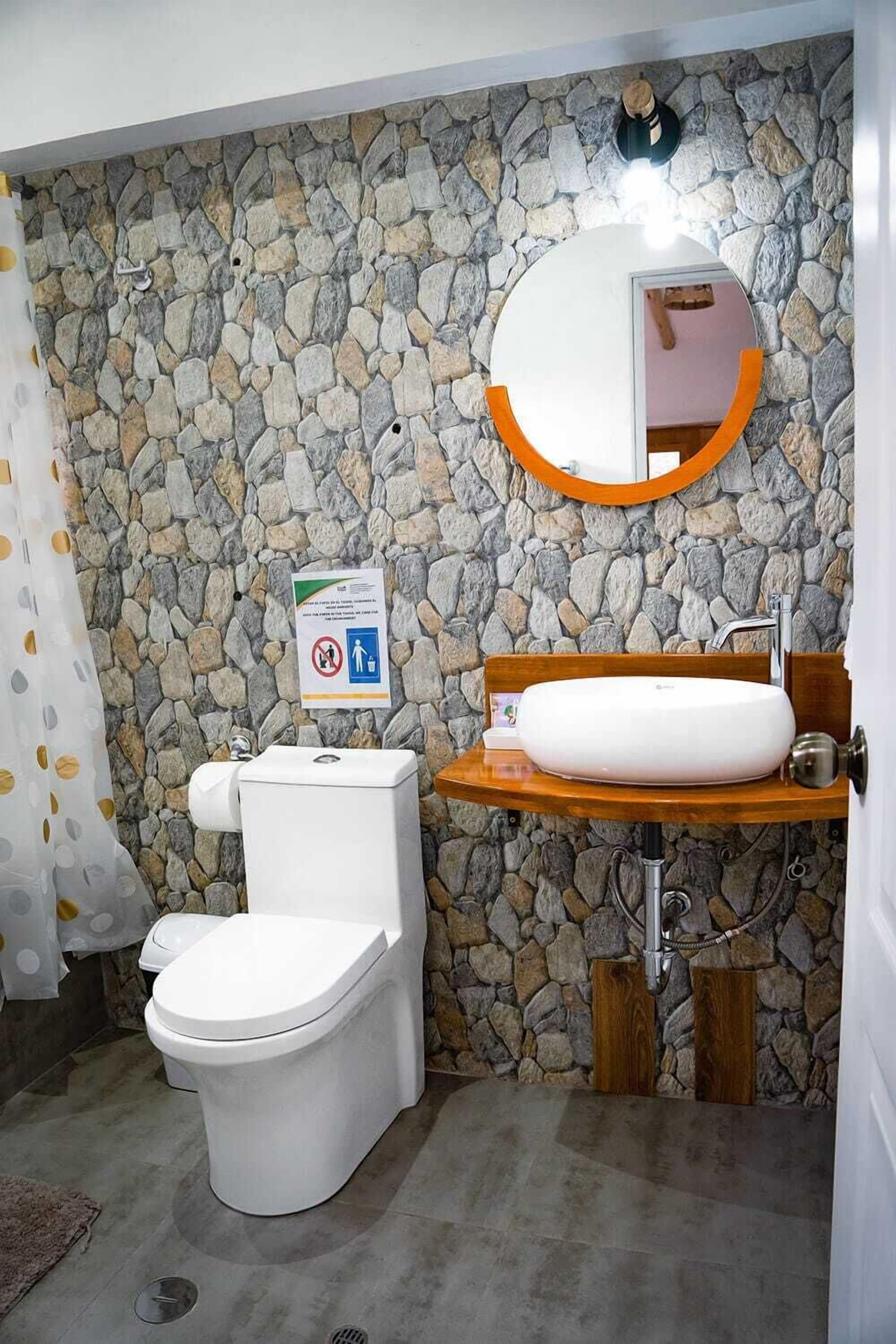 Een badkamer met een stenen muur, een wit toilet, een houten wastafel en een spiegel met oranje lijst.