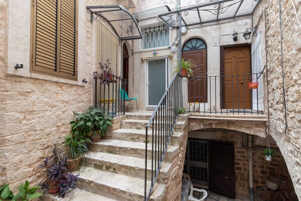 A stone staircase leading to a door with a window above, surrounded by potted plants and a metal railing.
