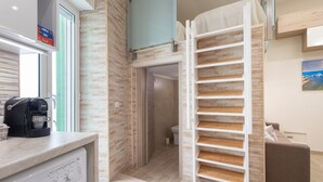 Une cuisine moderne équipée d’une machine à café, d’un lave-linge et d’un escalier blanc menant à une chambre à coucher située en mezzanine.