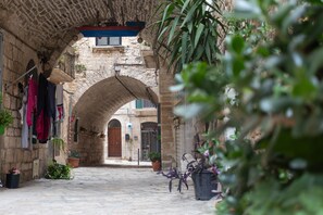 An arched stone alleyway with hanging clothes, potted plants, and a bicycle.