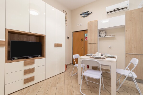 Una cocina moderna con televisor de pantalla plana, armarios blancos, encimera de madera y un comedor con sillas blancas.