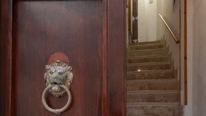 Une porte en bois ornée d’une tête de lion servant de heurtoir, et un escalier en pierre muni d’une main courante.