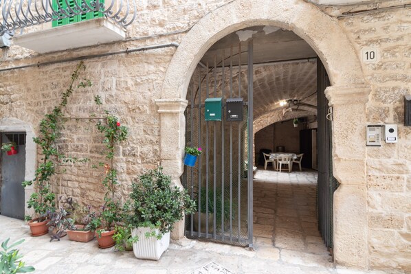 A stone building with an arched entrance, potted plants, and a number '10' sign.
