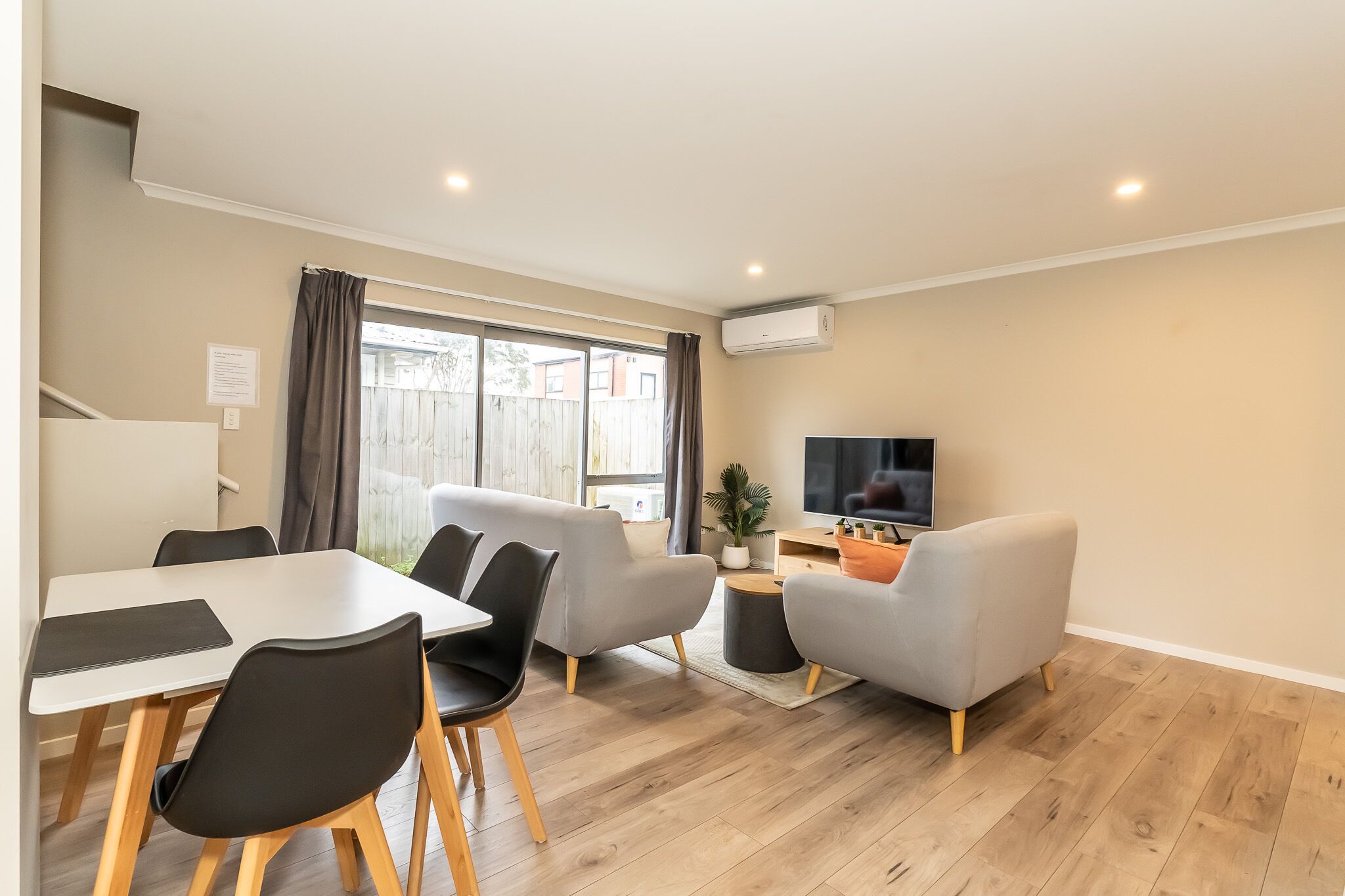 A modern living room with a dining table, chairs, a sofa, a TV, and an air conditioning unit.