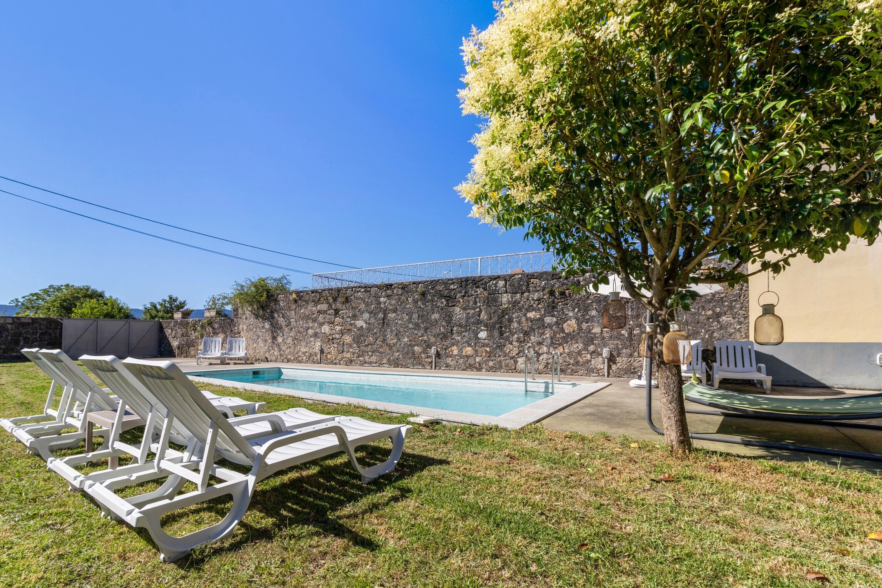 A swimming pool with lounge chairs, a tree, and a stone wall.