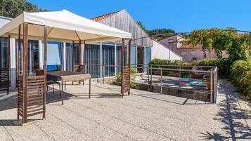 Un patio al aire libre con mesa y sillas, una zona de estar techada y una piscina.
