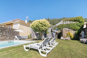 Un espace piscine avec des chaises longues, un mur en pierre et un arbre.
