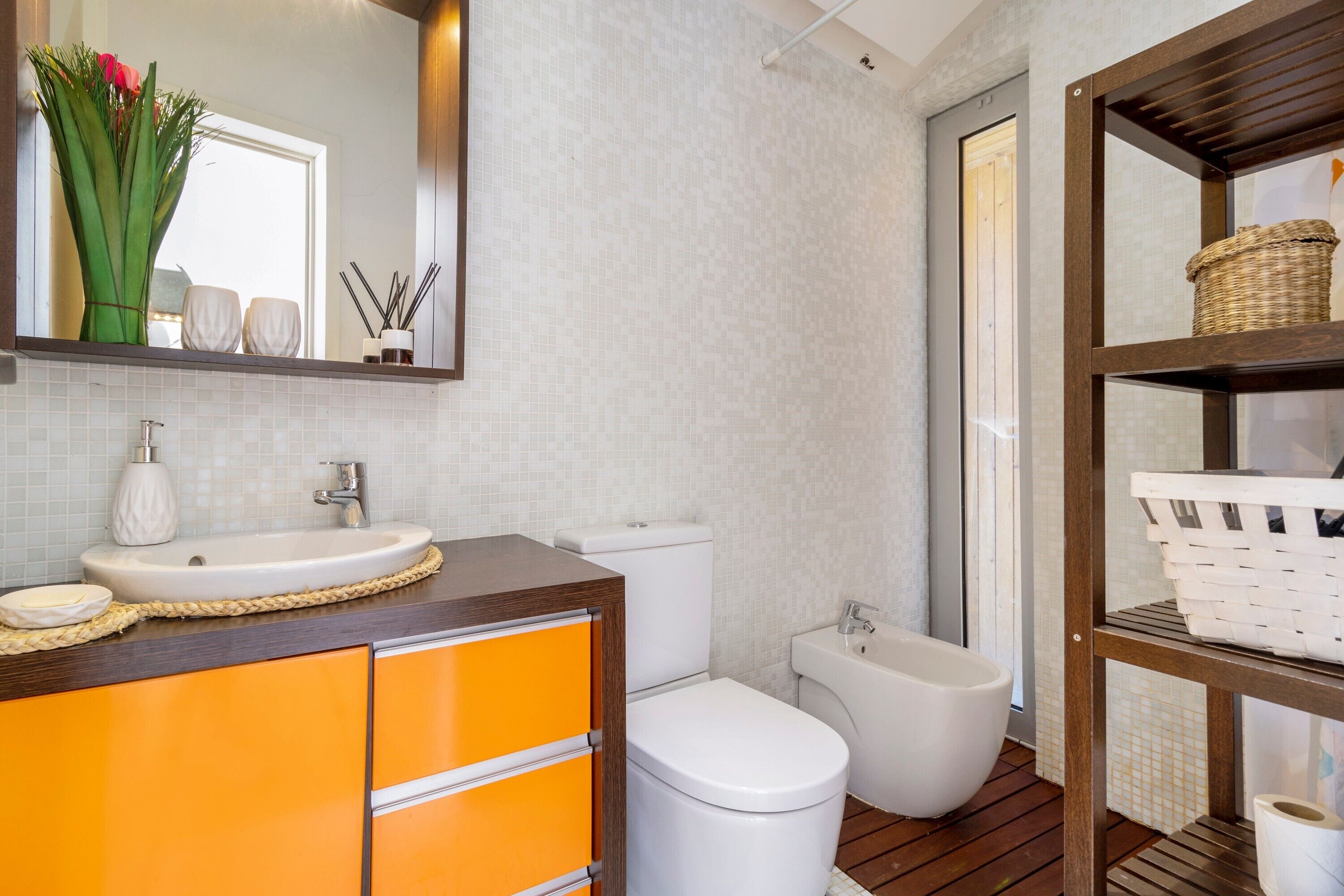 A bathroom with a white sink, orange cabinets, a white toilet, a bidet, and a wooden floor.