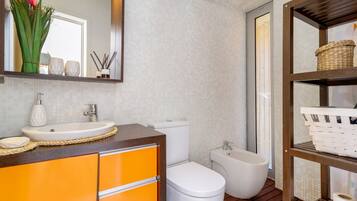 A bathroom with a white sink, orange cabinets, a white toilet, a bidet, and a wooden floor.