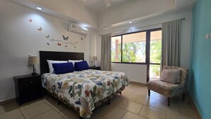 Una camera da letto con un letto, comodini, una sedia, una ventola a soffitto e una finestra con tende.