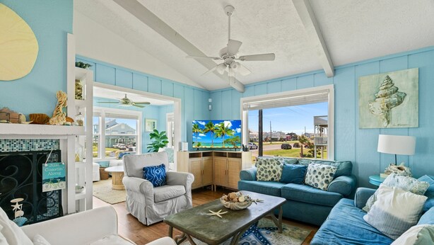 A living room with a view of the ocean, a ceiling fan, and a fireplace. - Escape by the Sea! NEW! (Galveston)