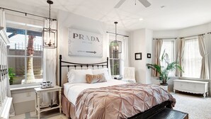 A bedroom with a bed, a nightstand, a dresser, a ceiling fan, and a window with curtains. - Cozy Garden Apartment | Heated Pool Access (Savannah)