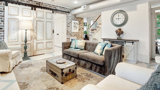 A living room with a brown sofa, a white armchair, a coffee table, and a vintage trunk. - Cozy Garden Apartment | Heated Pool Access (Savannah)