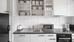Eine moderne Küche mit weißen Schränken, einem Edelstahl-Kühlschrank, einer integrierten Mikrowelle, einer Kaffeemaschine und einem Toaster.